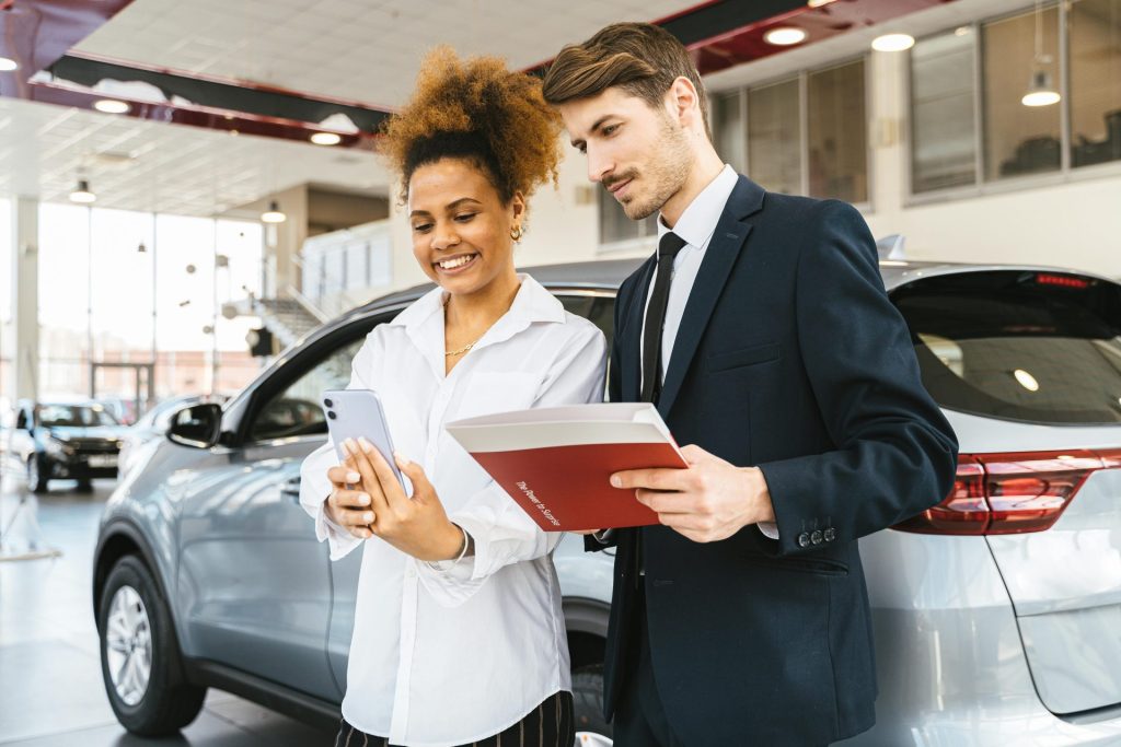 Una mujer y un hombre sonriendo mientras revisan detalles en un concesionario de automóviles. Ideal para imágenes de negocios o estilo de vida.